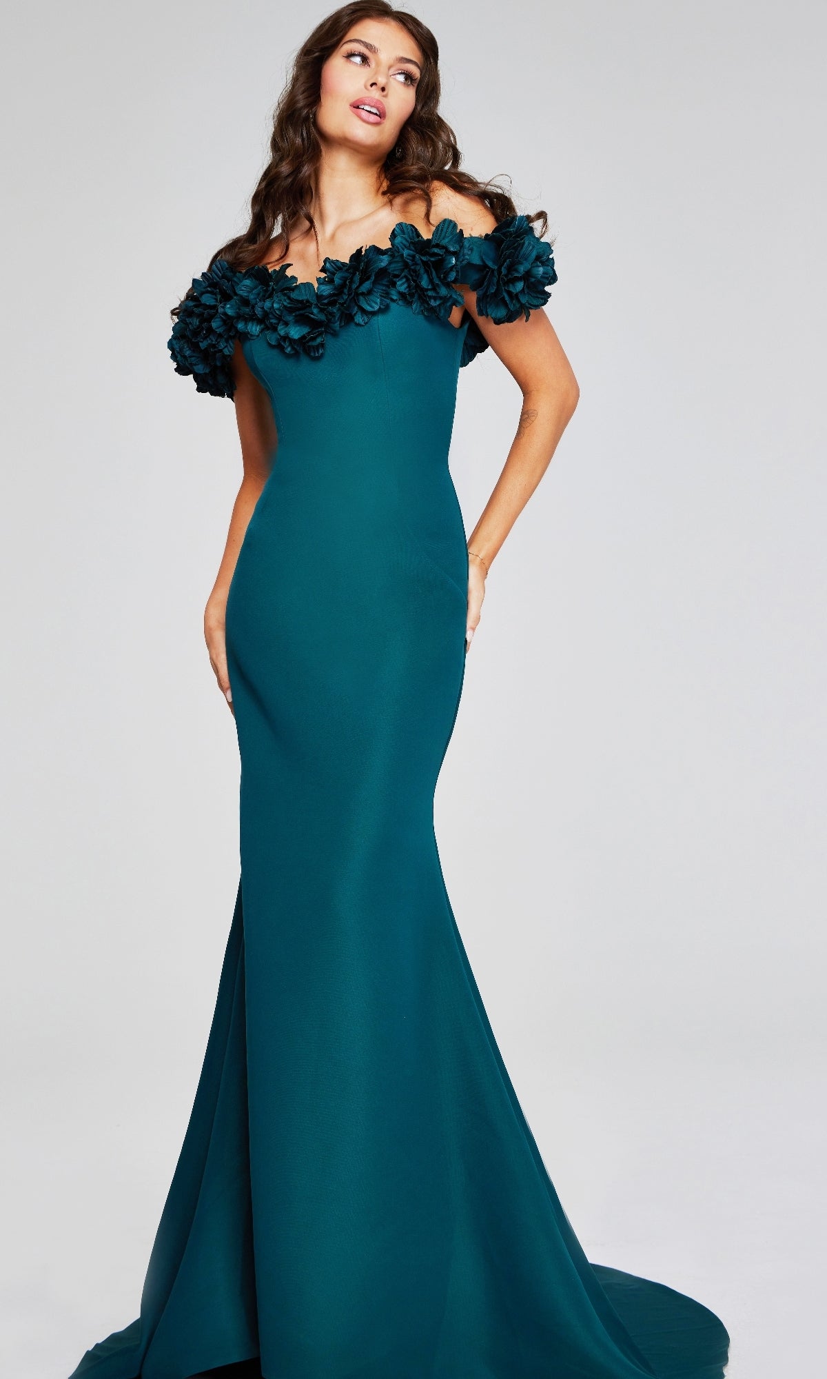 A woman models the Jovani 40595 long formal dress—a fitted, floor-length teal designer gown featuring off-the-shoulder floral details—against a plain background.